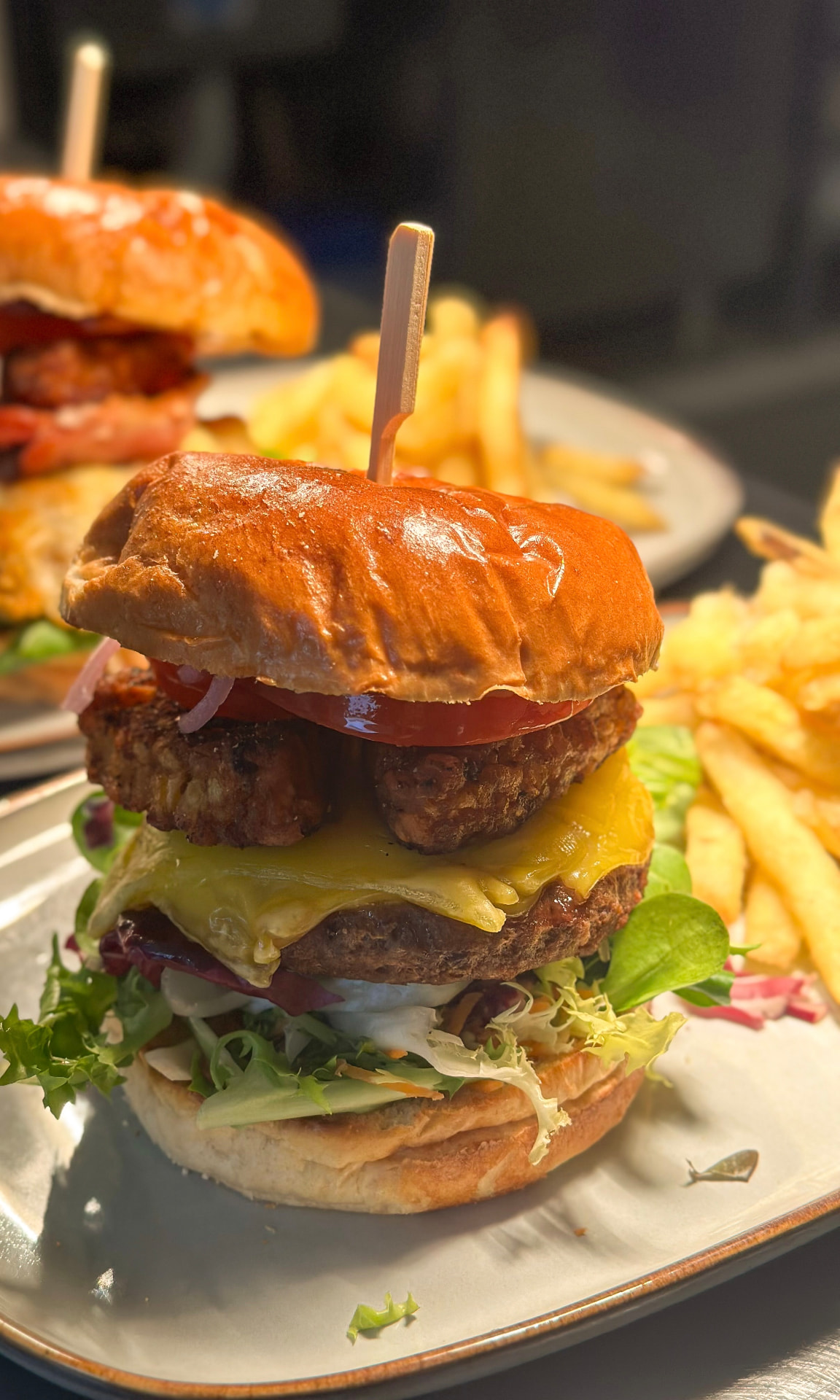 Stacked Louisiana burger with melted cheese, tomato and fresh leaves, served with fries